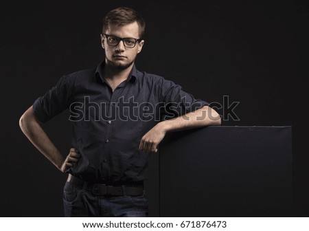 Young serious man portrait of a confident businessman showing presentation, pointing paper placard black background. Ideal for banners, registration forms, presentation, landings, presenting concept.