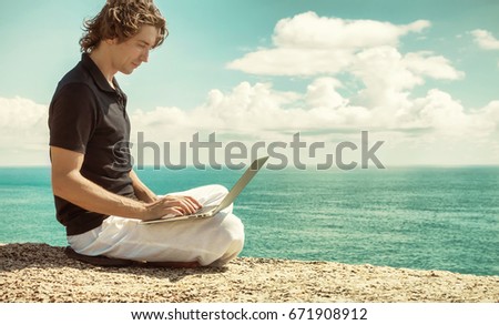 Man working with laptop sitting on the rocky mountain on beautiful clouds seascape background. Freelance concept.