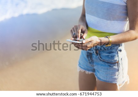 Hipster girl hold on smart phone gadget in sand coastline, mock up of screen. Traveler using in female hand mobile on background beach seascape horizon. Tourist look on blue sun ocean, lifestyle 