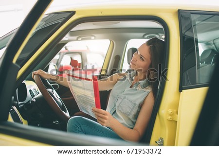 beautiful young woman buying a car at dealership. Female model sitting inside vehicle in showroom.