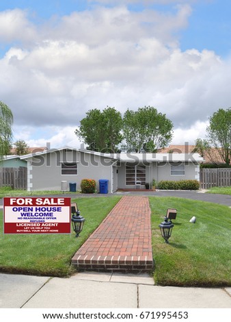 Rea; Estate for sale sign gray suburban ranch style home brick walkway blue sky clouds USA