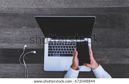 Top view Businessman's hands using smartphone and laptop on grey wooden table at office.