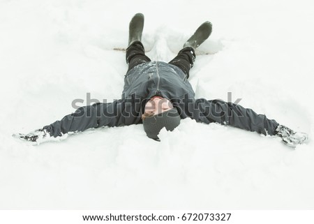 View from head of child laying flat in snow trying to make angel shapes by moving legs and arms up and down