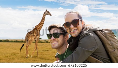 travel, tourism and people concept - happy couple in sunglasses with backpacks over african savannah and giraffe background