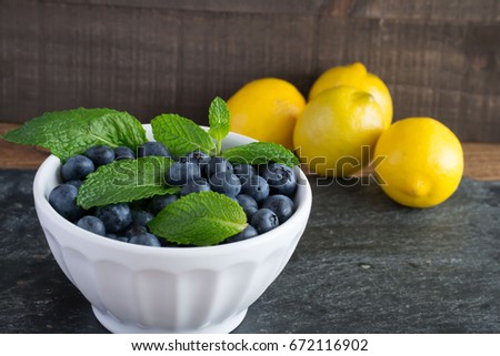 Blueberries in a white bowl with green mint and yellow lemons-vertical orientation