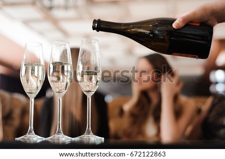 Man fills glasses of champagne for three beautiful young women in restaurant