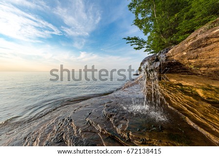 Elliot Falls spills over sculpted rock at Pictured Rocks National Lakeshore in Munising Michigan. This little waterfall is on Miner's Beach and sunrise skies light the background