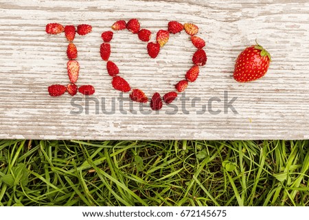 Strawberries are laid out in the letters on a background of green grass and board.