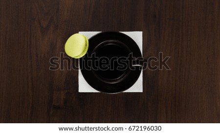 Brown cup of coffee with green macaroon on the wooden table and napkin.