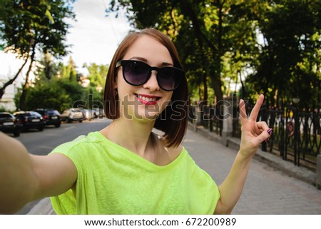 Pretty young woman in sunglasses taking selfie and showing two fingers