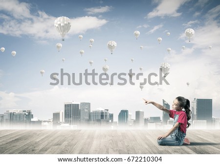 Cute kid girl sitting on wooden floor and aerostats flying in air