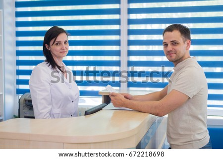 Mid adult female receptionist receiving card from patient in dentist clinic