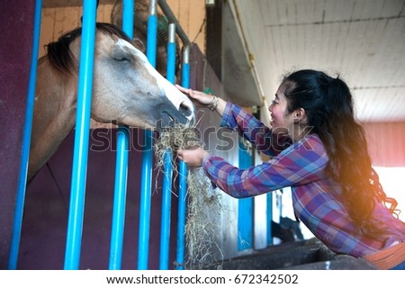 Pretty Asian woman petting horse in a farm.