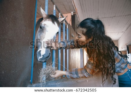 Pretty Asian woman petting horse in a farm.