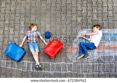 Two little kids boys having fun with train picture drawing with colorful chalks on ground. Children having fun with chalk and crayon painting and game going on vacations. Friends with suitcases.