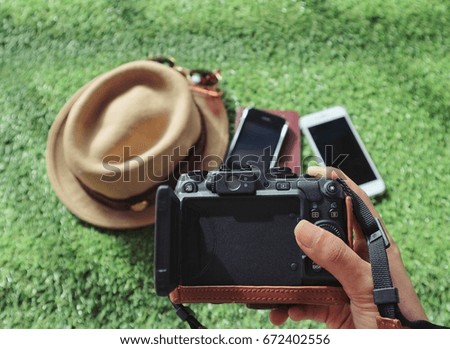 Holiday vacation concept , hand hold camera leather case, phone, passport book and hat on green grass natural