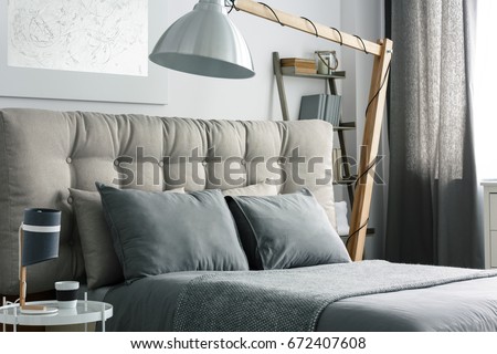 Grey bed with quilted headboard and big wooden lamp Royalty-Free Stock Photo #672407608