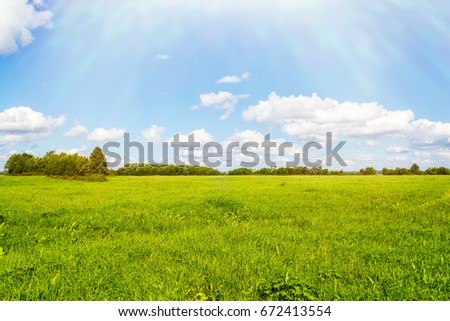 Green field, blue sky, bright clouds and sun Royalty-Free Stock Photo #672413554