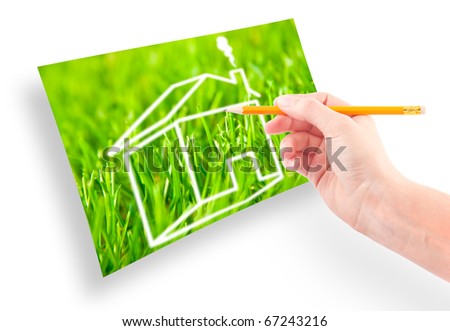 Hand of a girl with a pencil draws a house against on the green grass.