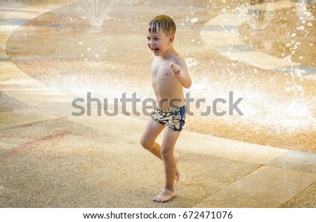 Cute happy Caucasian child running through the water stream of a sprinkler in the summer heat. Summer fun stock image.