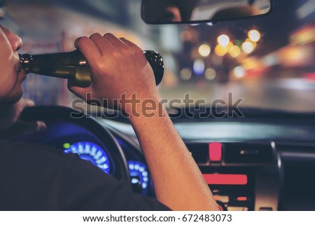 Man drink beer while driving at night in the city dangerously, left hand drive system Royalty-Free Stock Photo #672483073