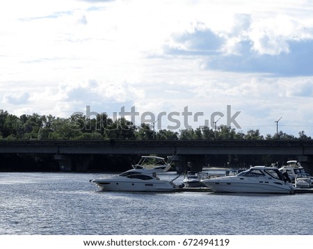 Motor boats on the pier on a river under a blue sky and clouds.  