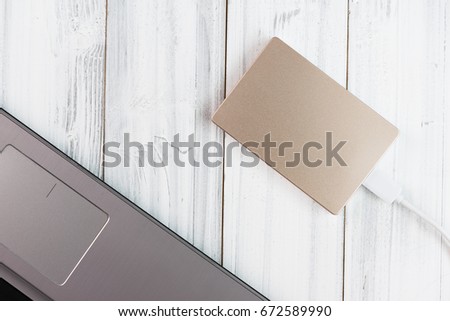 Flat lay  bronze color external hard drive connect to laptop computer on white wooden background,top view