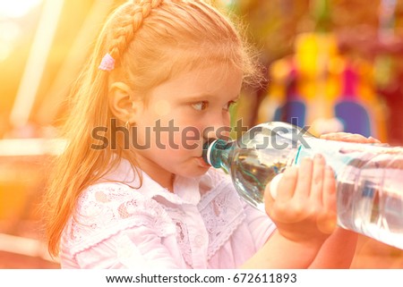 I am Thirsty. Closeup portrait little cute girl drinking mineral water from her bottle isolated outside, outdoors park background. Retro toned, orange golden sunset