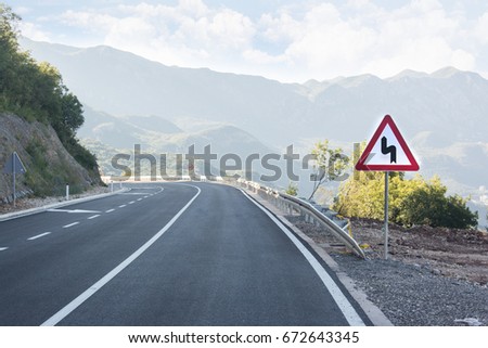 Asphalted mountain road with sharp sharp turn near the cliff. Traffic sign