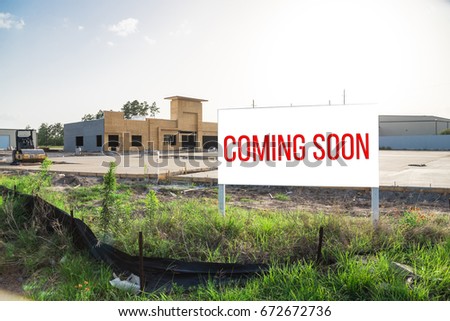 Coming Soon sign stands at the street corner/intersection, under construction convenience store is in background. Signboard with the words Coming Soon outdoor for brand new gas station soon open.