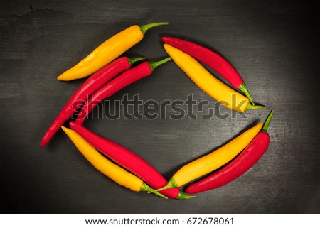Red and yellow chilli peppers forming a frame on a black texture, shot from above with a place for text