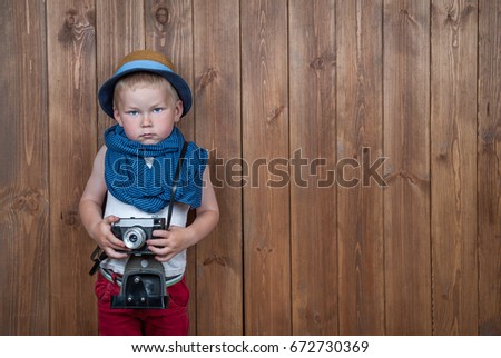 Cute toddler boy with old retro camera on vintage wooden boards abstract background.  Child  with blue eyes in straw hat playing with photo