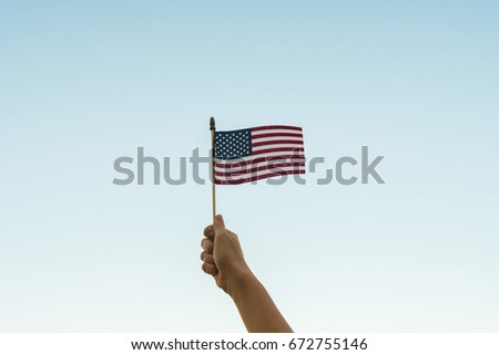 Hand holding American flag in air against sky