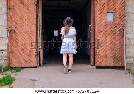 A girl in a white dress and a cowboy hat dancing against the backdrop of a horse at the ranch