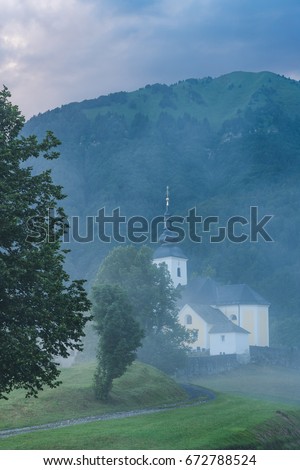 Parish Church sv.Nikolaja in Sorica, Slovenia at misty day with mountains in background.