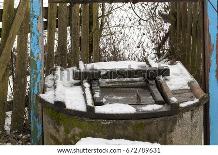  photo of an old well in a village covered with snow falling during a snowfall