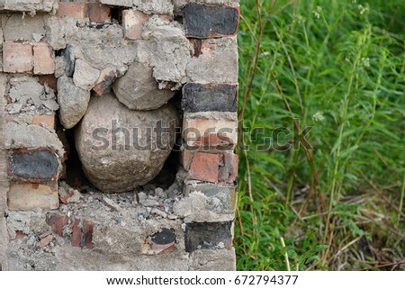 A fragment of burnt brick walls is filled with large stones inside, more grass