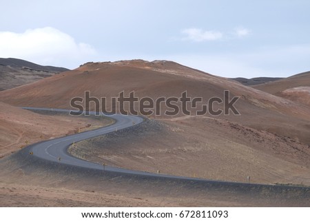 empty road going through geothermal volcanic zone, traveling by car, typical icelandic landscape - cloudy sky, grey hills, volcanic desert, Myvatn area, Hverir, Iceland 