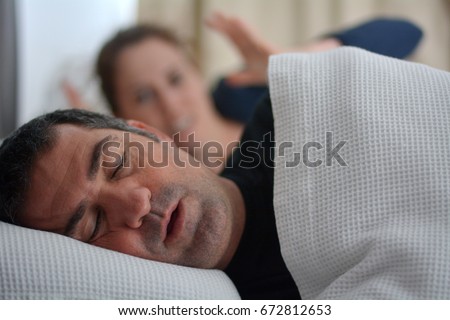 Woman (female age 30) suffers from her male partner (man age 40) snoring while lying in bed together. Snoring is one of the factors of sleep deprivation. Noise concept. Real people. Copy space  Royalty-Free Stock Photo #672812653
