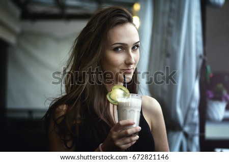 Outdoor closeup portrait of pretty stylish fashion woman in evening dress drinking chocolate milkshake with kiwi fruit in a cafe outdoors. Lifestyle photo with backlight and smooth background