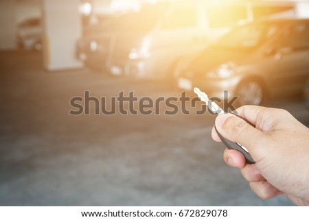 Hand holding car key remote at car park background