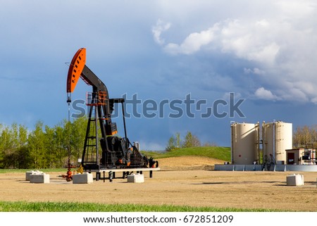 New Oil pumper,extracting oil, in a remote rural area of Alberta, Canada, with storage tanks in the background 