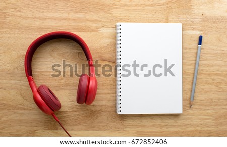 Red headphone, notebook and pencil on wooden table.
