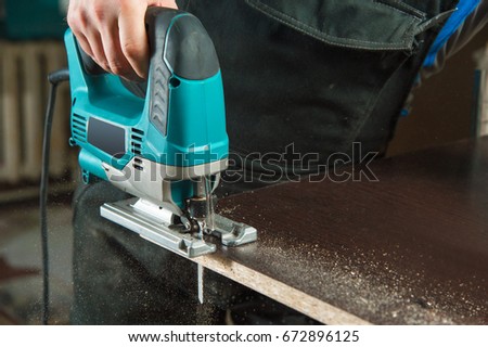 Close-up carpenter working with an electric jigsaw Royalty-Free Stock Photo #672896125