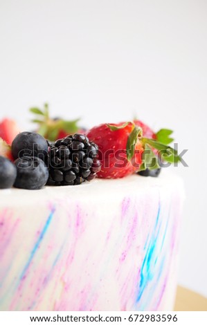 Cake with whipped blue and pink cream, fresh strawberries, blueberries and blackberry. Close-up. Picture for a menu or a confectionery catalog.