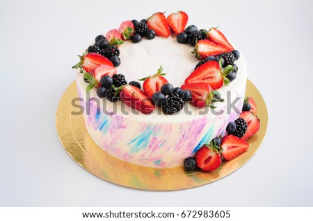 Cake with whipped blue and pink cream, fresh strawberries, blueberries and blackberry. Picture for a menu or a confectionery catalog.