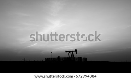 Silhouette of crude oil pump in oilfield at sunset blue hour - black and white 