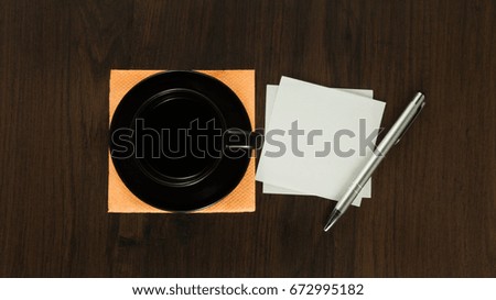 Brown cup of coffee with pieces of paper silver pen on the wooden table and napkin.