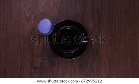 Brown cup of coffee with blue macaroon on the wooden table.