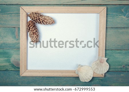 Blank photo frame with pine cones and sea shells on wooden background